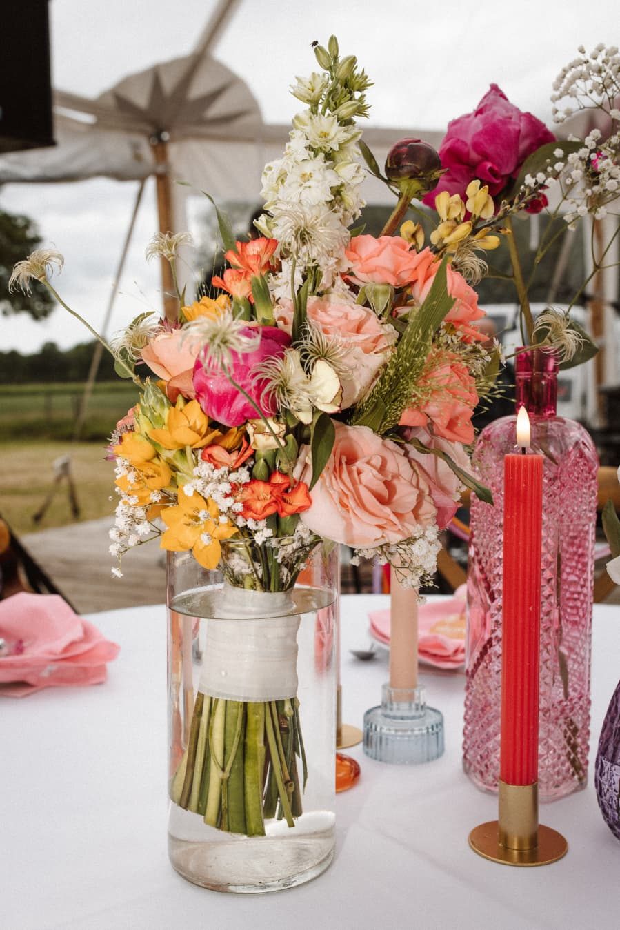Kleurrijk boeket en roze kaarsen op een gedekte tafel
